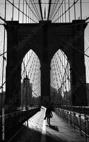Brooklyn Bridge travel lifestyle, a woman walking along the historic pedestrian path beneath iconic suspension cables, Lower Manhattan, New York City, USA.