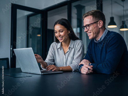 Tableau sur toile Happy diverse colleagues collaborating and smiling while working together on a laptop in a modern office