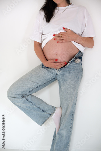 Pregnant Woman in Jeans and White T-Shirt Posing Near Wall
