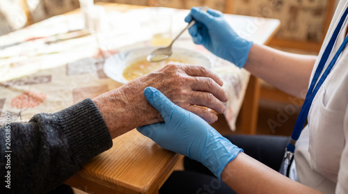 Caregiver providing assistance for an elderly person, feeding them soup and offering emotional support with a gentle touch
