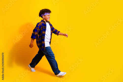 Obraz na plátne Happy young boy walking confidently across a bright yellow studio background in