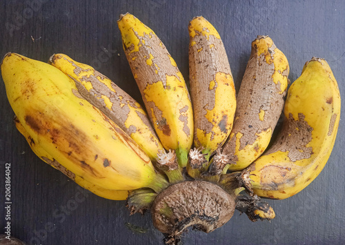 bunch of bananas with some fruits already taken, placed on a dark wooden board and photographed from above