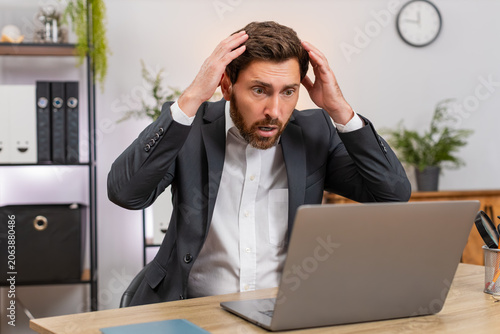 Foto Middle-aged businessman at home office watches laptop freeze eyes widen and presses keys to save work before reboot
