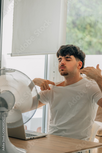 young man at home studying and working on a laptop during a summer heat wave