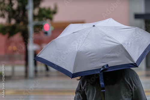 Tableau sur toile Undersized two‑toned UV umbrella speckled with rain shields a person paused at a crosswalk as a red signal glows softly ahead during an unexpected drizzle