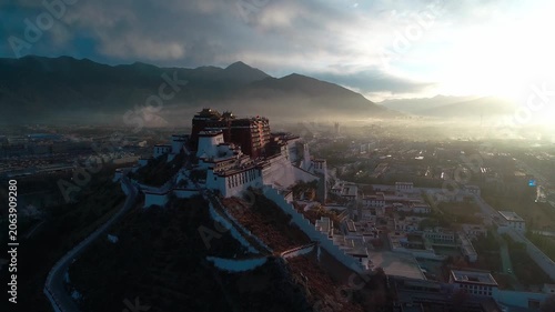 Aerial view of the Potala Palace at sunrise in Lhasa, Tibet, China, with the historic palace on the hill overlooking the city, surrounded by mountains and morning mist under golden light.