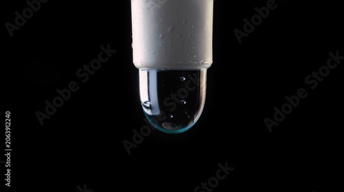 A close-up macro photo of green liquid slowly dripping from the end of a syringe