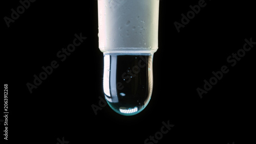 A close-up macro photo of green liquid slowly dripping from the end of a syringe