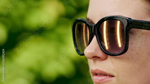 Woman wearing sunglasses with urban reflection in lenses. Profile view of caucasian girl with freckles outdoors. Summer eyewear fashion accessory style concept
