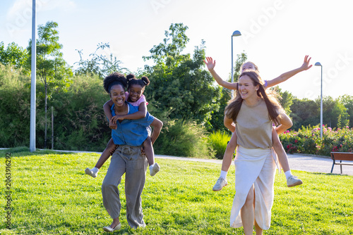 Cuadro en lienzo Diverse mothers giving daughters piggyback rides in park