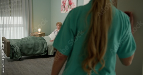 Fotografie Elderly woman lying in bed with nurse standing nearby