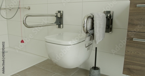 Modern bathroom featuring wall-mounted toilet, safety support bars, and towel. Accessible and functional design promoting independence and safety