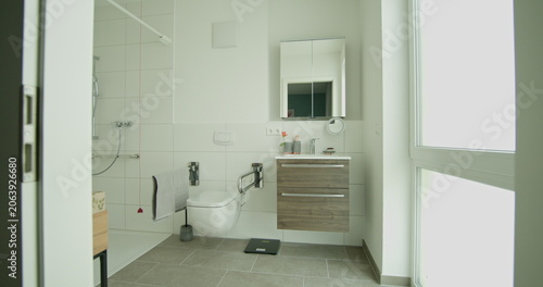 Contemporary bathroom with wheelchair accessible shower and modern vanity. White tiles and natural light create clean and bright space. Design includes accessible features for ease of use.