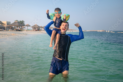Joyful father and son playing in the sea, beach setting, sunny d