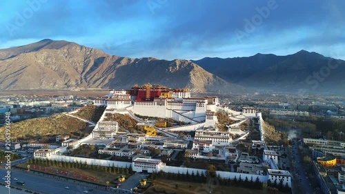Aerial view of the Potala Palace at sunrise in Lhasa, Tibet, China, with the historic palace on the hill overlooking the city, surrounded by mountains and morning mist under golden light.