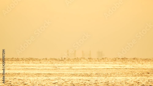 Ocean mirage horizon shimmering heat haze over the sea at sunset with distant industrial structures and a flying bird