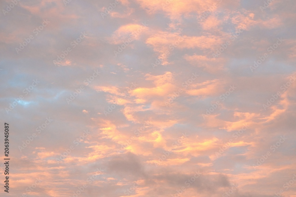 Fototapeta premium Soft pastel clouds illuminated by sunset light in a colorful evening sky. Atmospheric cloudscape background with warm tones, natural beauty and ample copy space.