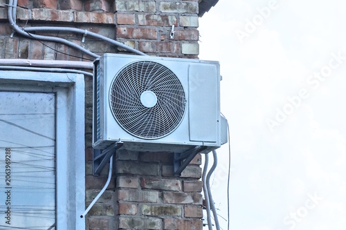 one white big fan hanging on a brown brick wall of a building on the street
