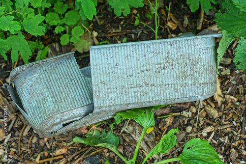 A long gray plastic broken flowerpot lies on the ground in green vegetation on a summer street