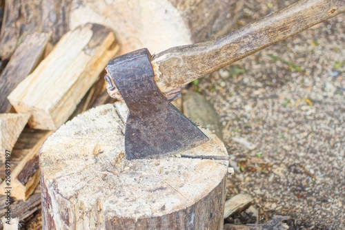one big old brown axe sticks out of a piece of cut log on the gray ground on a daytime street
