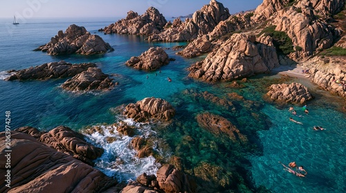 Summer sun sets over Sardinia's rocky coast. Swimmers enjoy transparent blue sea, with waves gently lapping at the shore.