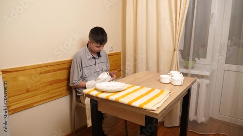 Teenager in a home kitchen drying and arranging clean dishes on a table, independently doing everyday household chores.