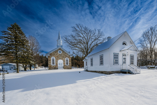 A snow-covered landscape with a church and a house under a clear blue sky.