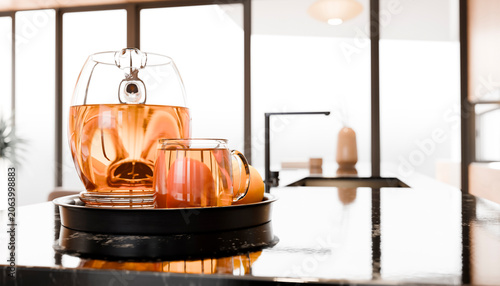 A glass teapot and cup with tea sit on a black countertop in a modern kitchen setting.