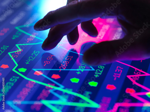 Hand touching a screen displaying a stock market graph with colorful data points.  