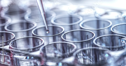 Close-up of a pipette dropping liquid into rows of transparent test tubes.