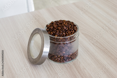 Coffee beans in glass jar on wooden table in the kitchen. Preparing for brewing coffee.