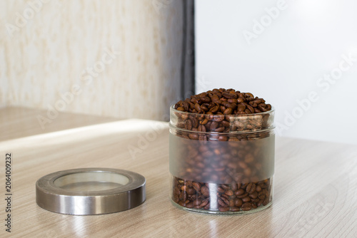 Open glass jar filled coffee beans on a table with natural light at home interior.