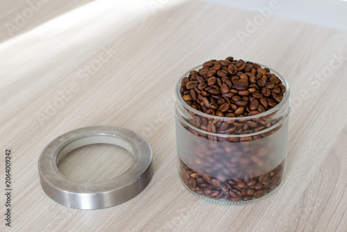 Glass jar filled with aromatic coffee beans rests on wooden surface. Preparing for brewing coffee.