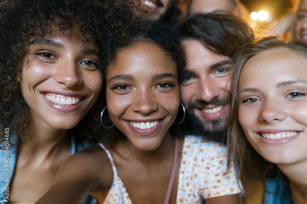 Fototapeta premium Warm group smiles fill the frame together. Close friends embrace joyful moments, eyes bright with laughter. Soft lighting highlights their happy expressions and natural beauty. Ideal for social events