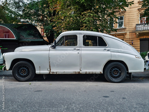 Old soviet classic  car abandoned white gaz-m20 Pobeda on Lviv city street in Ukraine, side view