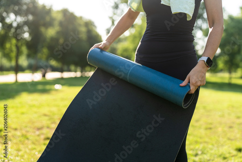 Woman folding and unfolding yoga mat in the park during sunset sunrise time.