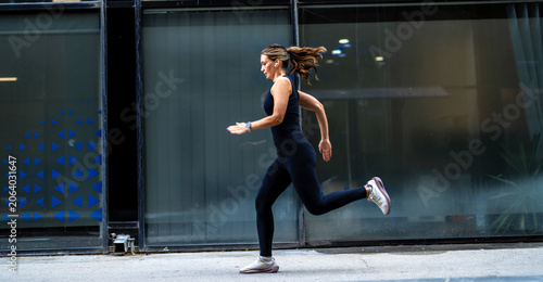 One young female athlete running on the spot while exercising outside in the city. Beautiful and dedicated mixed race sportswoman working out alone against an urban background.