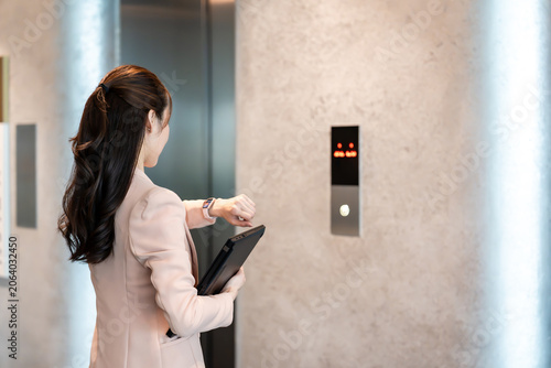 Close-up of a woman's hands holding a laptop while waiting for the elevator.