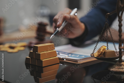 A dramatic, selective-focus close-up shot of a wooden judge's gavel being struck down onto its sound block. In the blurred background, a lawyer in a dark suit sits at a polished desk.  
