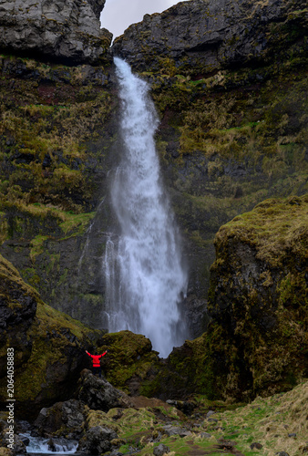 Hiker standing with arms raised, enjoying the powerful irafoss waterfall cascading down the mossy cliffs in iceland. Icelandic dramatic landscape