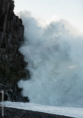 Powerful ocean waves impacting the dark basalt column cliffs at reynisfjara beach in iceland, creating dramatic spray and foam