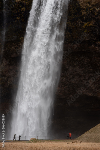 Seljalandsfoss waterfall cascading down the cliff, with people standing at its base, highlighting the immense scale and natural beauty of iceland. Icelandic landscape