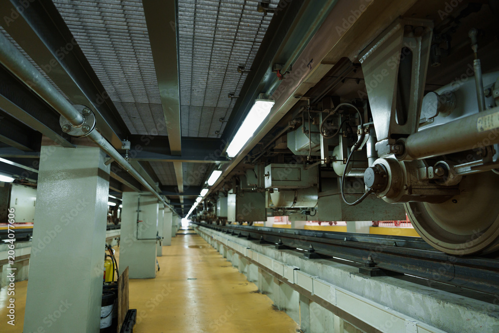 Obraz premium Dimly lit electric train car with large wheels rests on concrete subway tracks within cavernous underground station illuminated by warm overhead lights and sturdy support pillars.