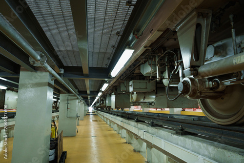 Dimly lit electric train car with large wheels rests on concrete subway tracks within cavernous underground station illuminated by warm overhead lights and sturdy support pillars.