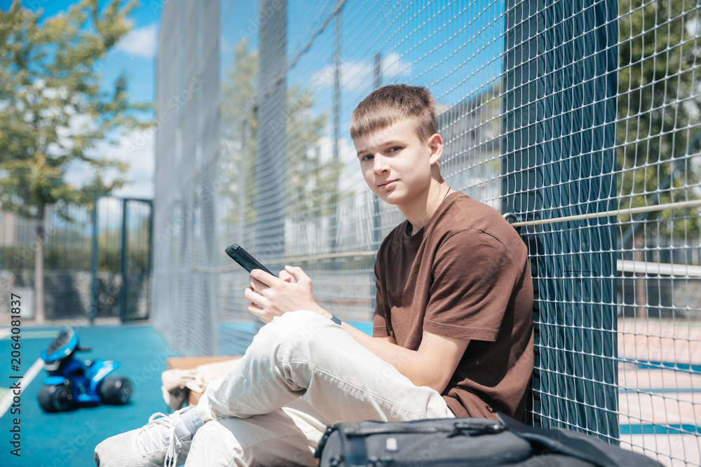 Obraz premium Teenager Enjoying a Sunny Day at the Park While Sitting on a Blue Court and Using His Smartphone With a Toy Nearby