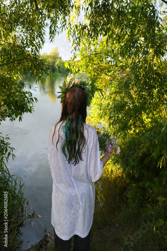 Young ault sitting near the lake water floating floral wreath with candle during Ivan Kupala