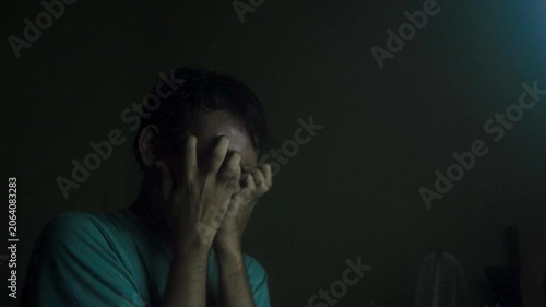 Depressed Young Man Covering Face With Hands In Dark Room Wearing A Teal Shirt Feeling Stressed