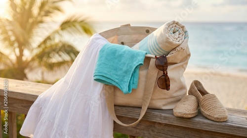 Beach bag with towel sunglasses and espadrilles on wooden railing by tropical sea at sunset