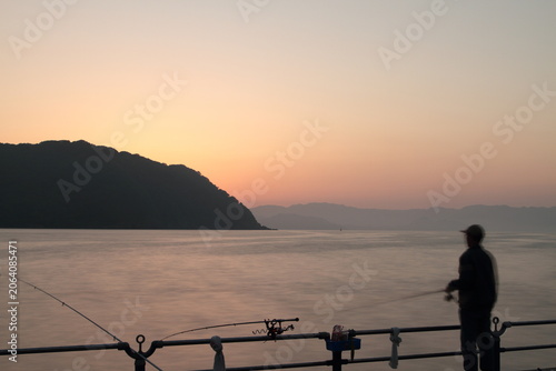 夕焼けに染まる海を眺める釣り人