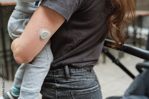 Close-up of a mom with type 1 diabetes holding her child on a walk, focusing on modern diabetes management tech. 